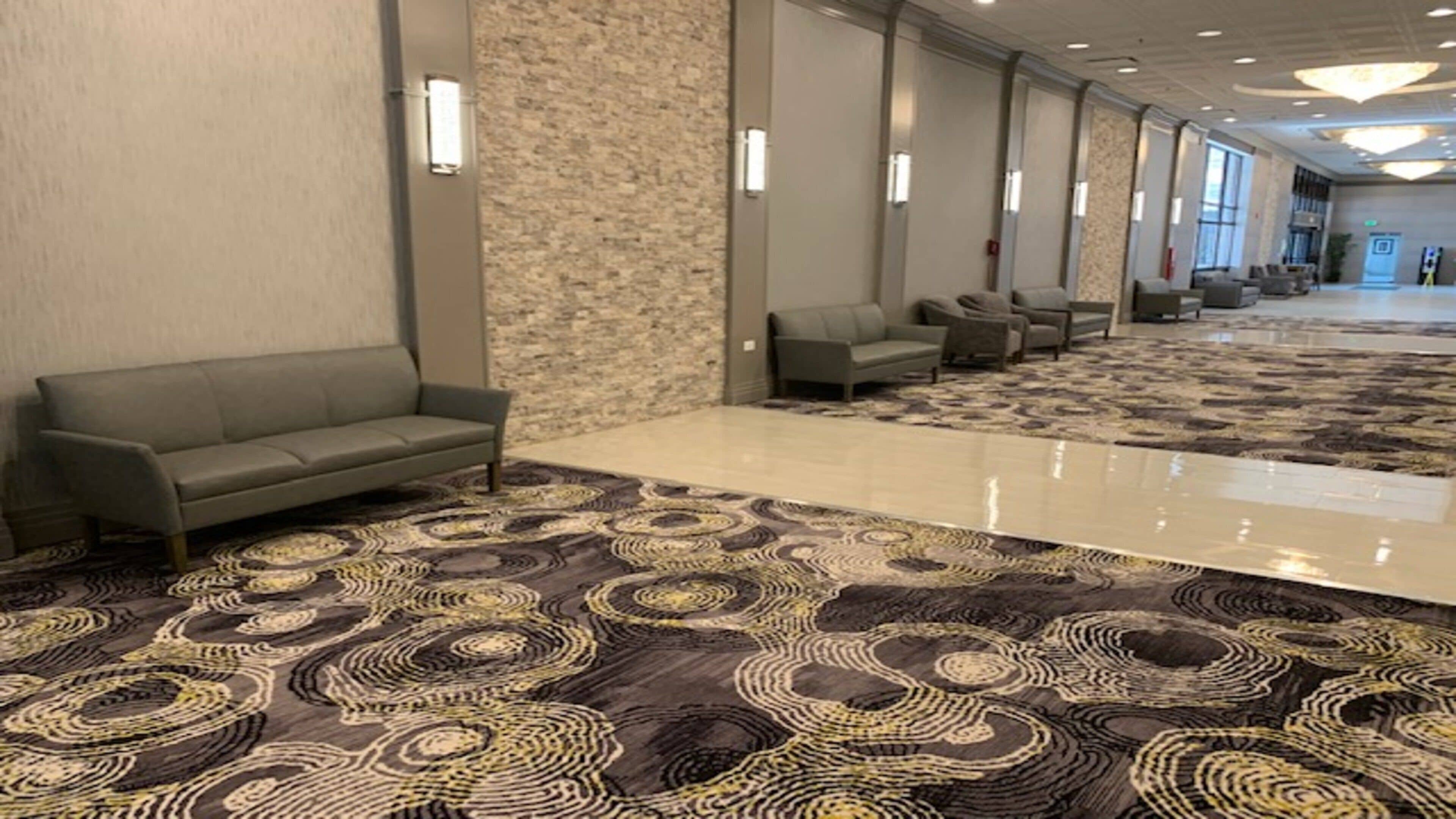 A hotel lobby with a patterned carpet, sofas, and a stone wall.