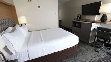Habitación de hotel con cama, escritorio, silla, televisor y cafetera.