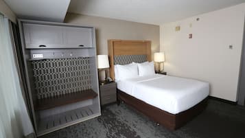 A hotel room with a bed, a wardrobe, a vanity with a mirror, and a nightstand with a lamp.