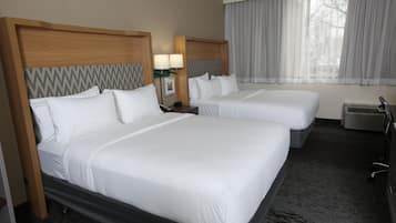 A hotel room with two beds, a nightstand with lamps, a window with curtains, and an air conditioning unit.