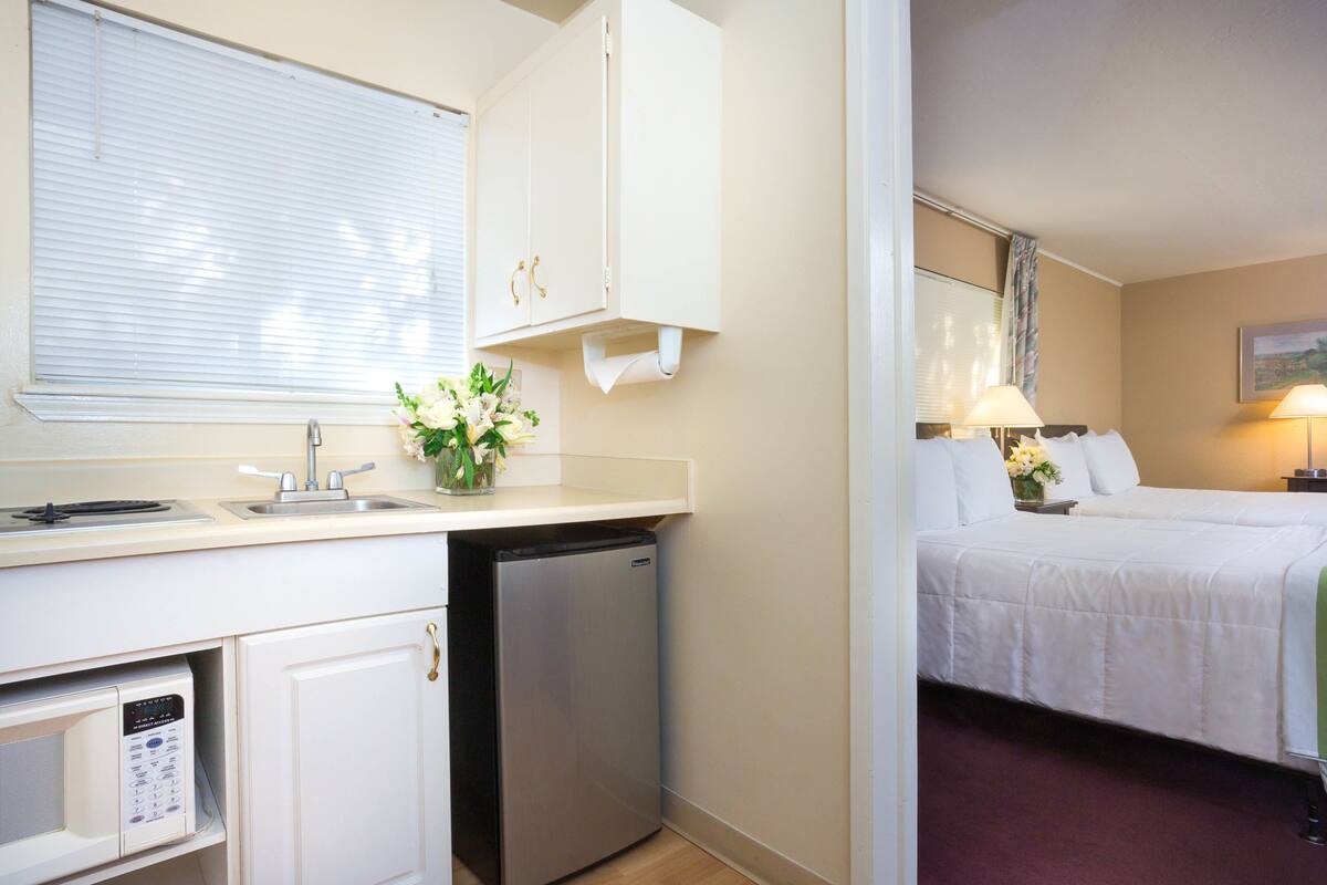 Une chambre d’hôtel compacte, dotée d’une kitchenette, d’un lit avec du linge de lit blanc et d’une petite salle de bain.