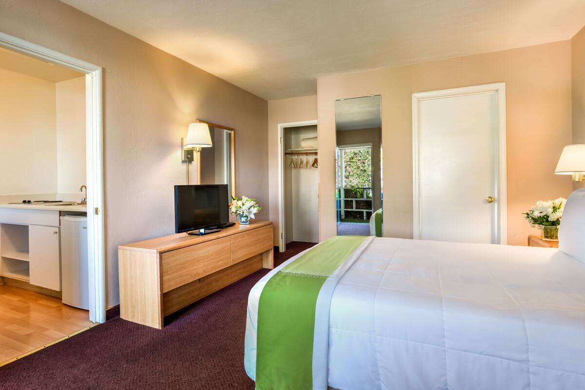 Une chambre d’hôtel comprenant un lit, un bureau avec une télévision, un miroir et une porte donnant sur un balcon.