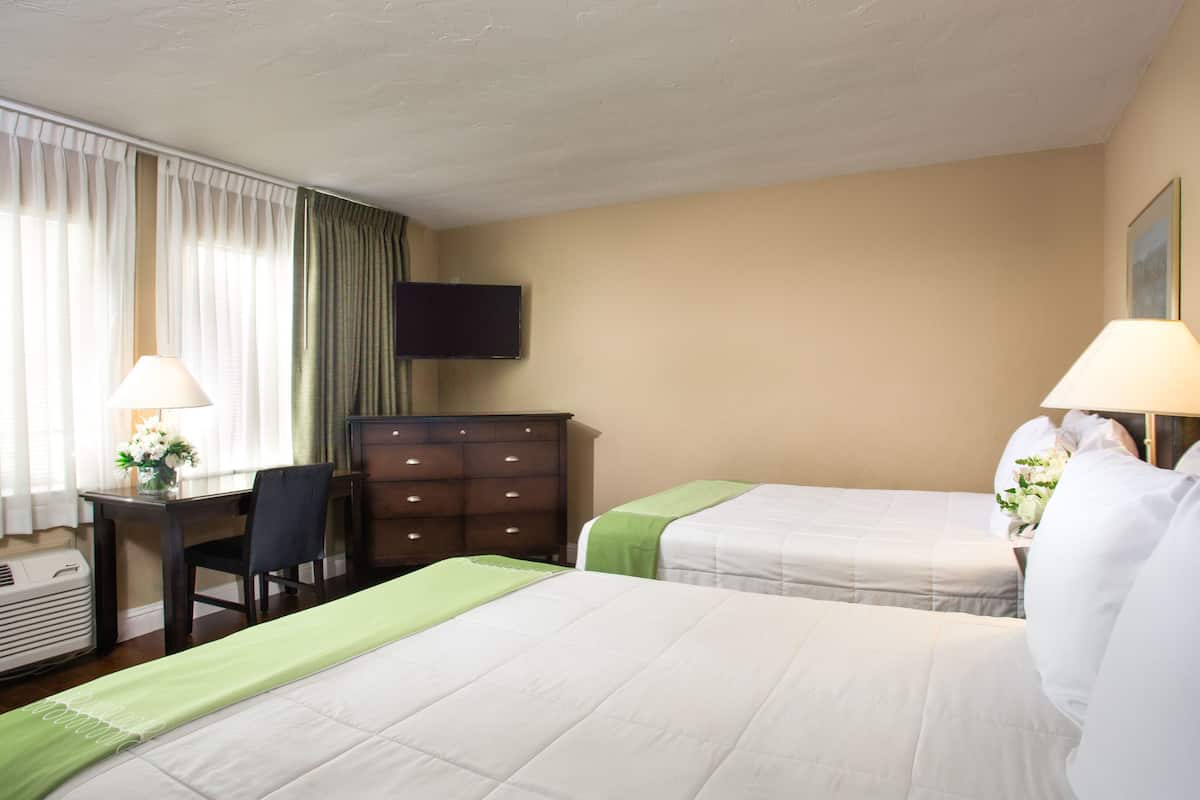 Une chambre d’hôtel avec deux lits, un bureau, une chaise, une commode et un téléviseur fixé au mur.