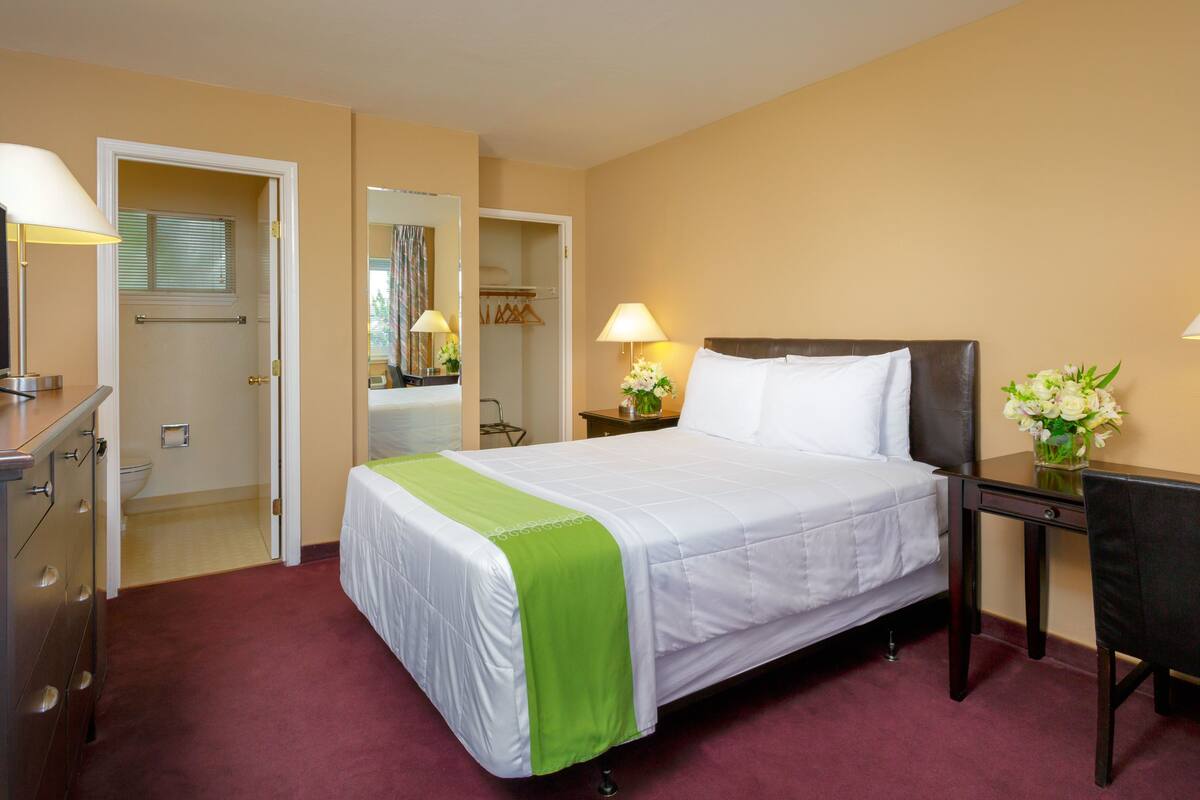 Une chambre d’hôtel comprenant un lit, une table de chevet, une lampe et un bureau avec une chaise.