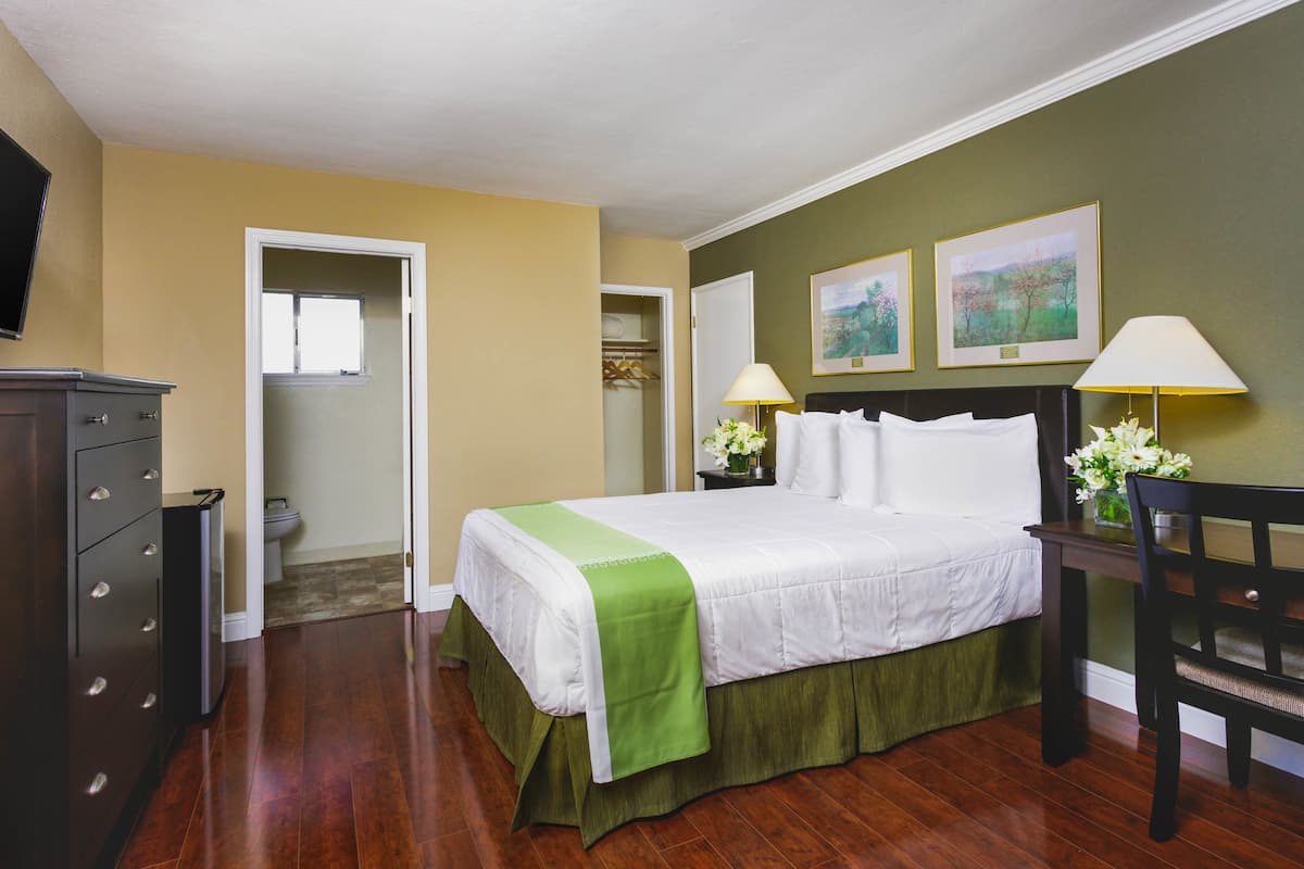 Une chambre d’hôtel avec un lit, des lampes de chevet, une commode, une chaise et un tableau au mur.