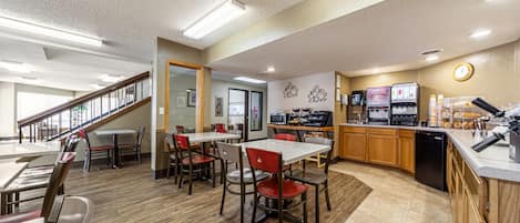 A spacious dining area with wooden flooring, a kitchen area with a coffee machine, and a staircase leading to another level.