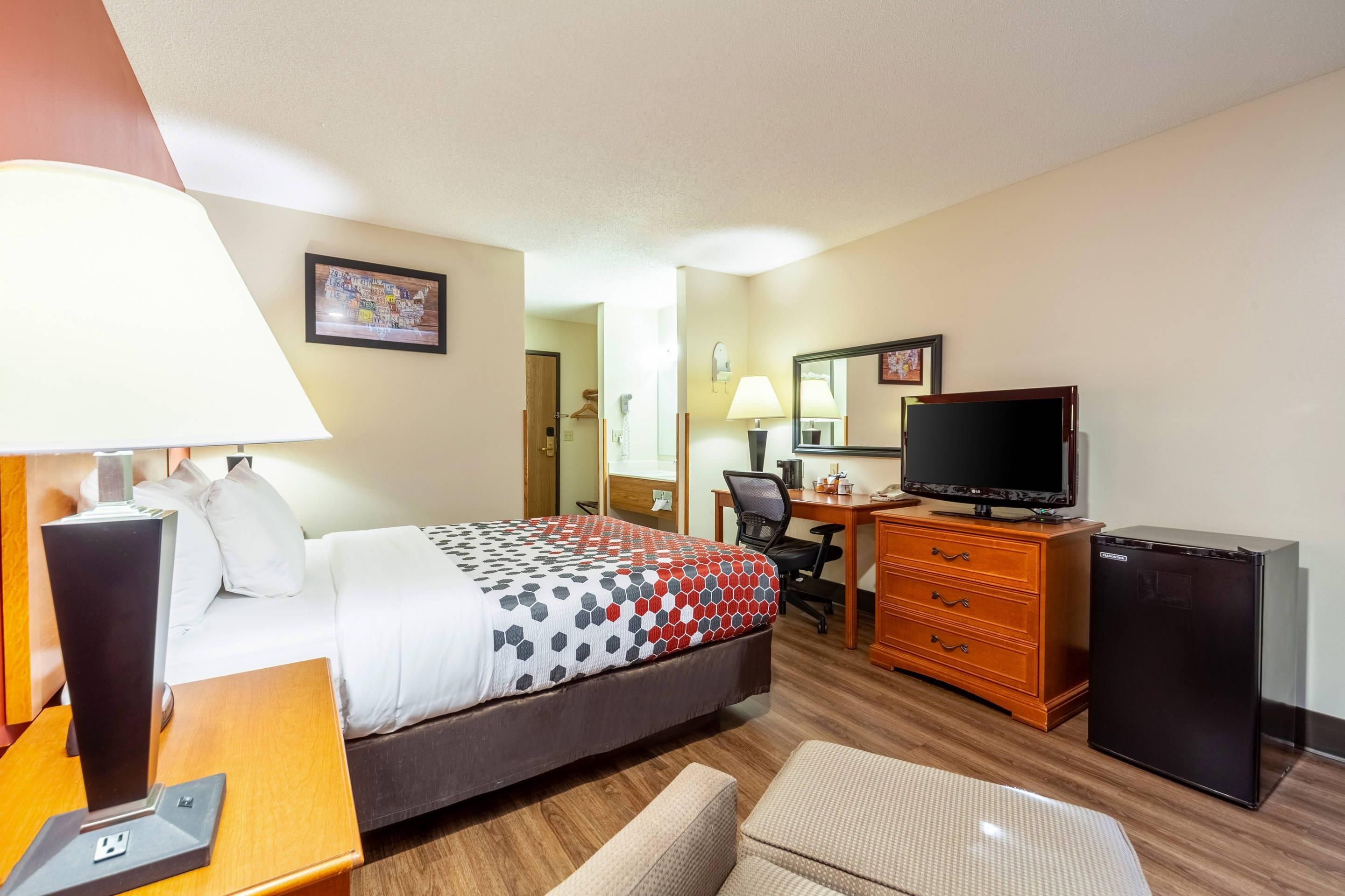 A hotel room with a bed, desk, chair, TV, and a small refrigerator.