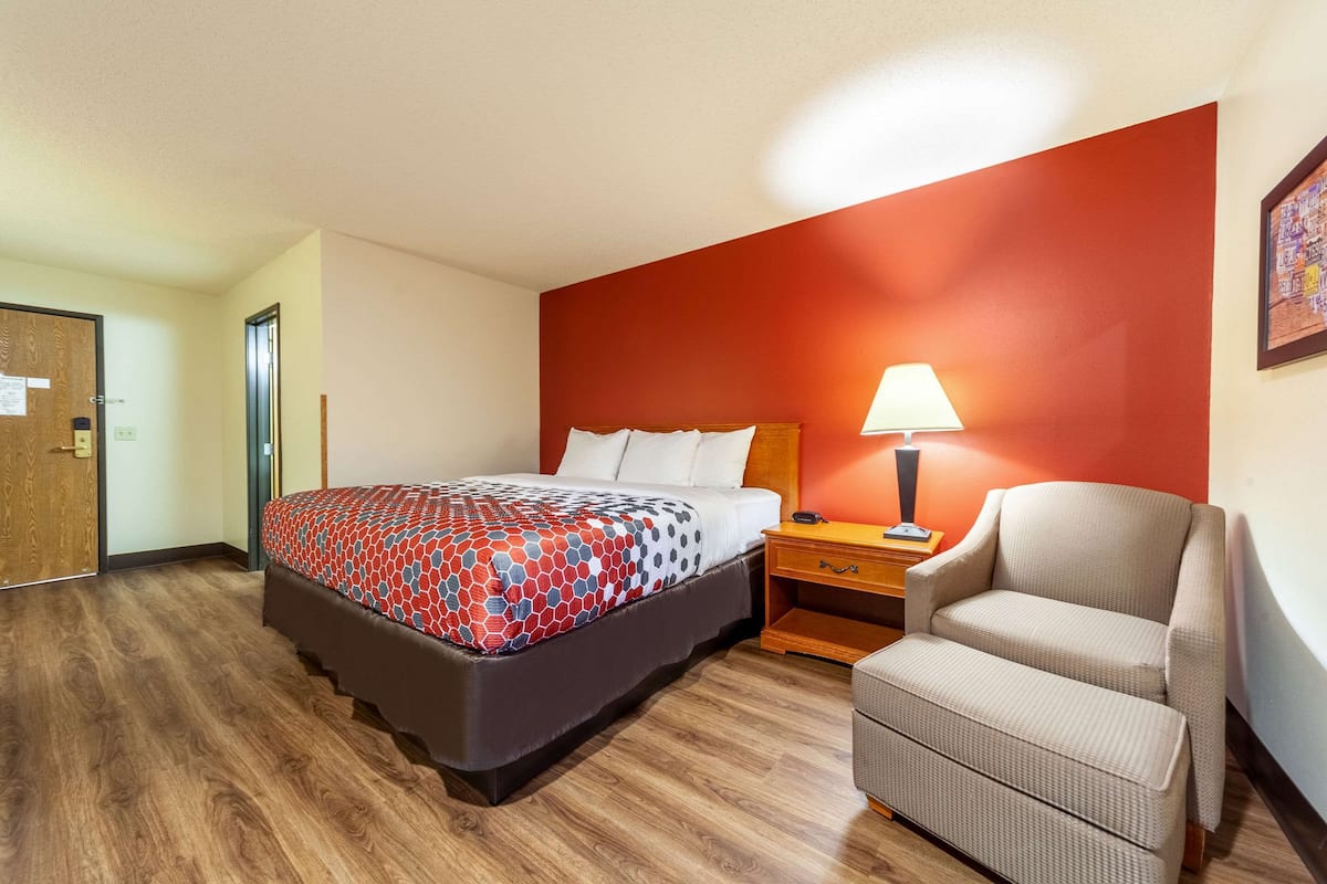 A hotel room with a bed, nightstand, chair, and a red accent wall.