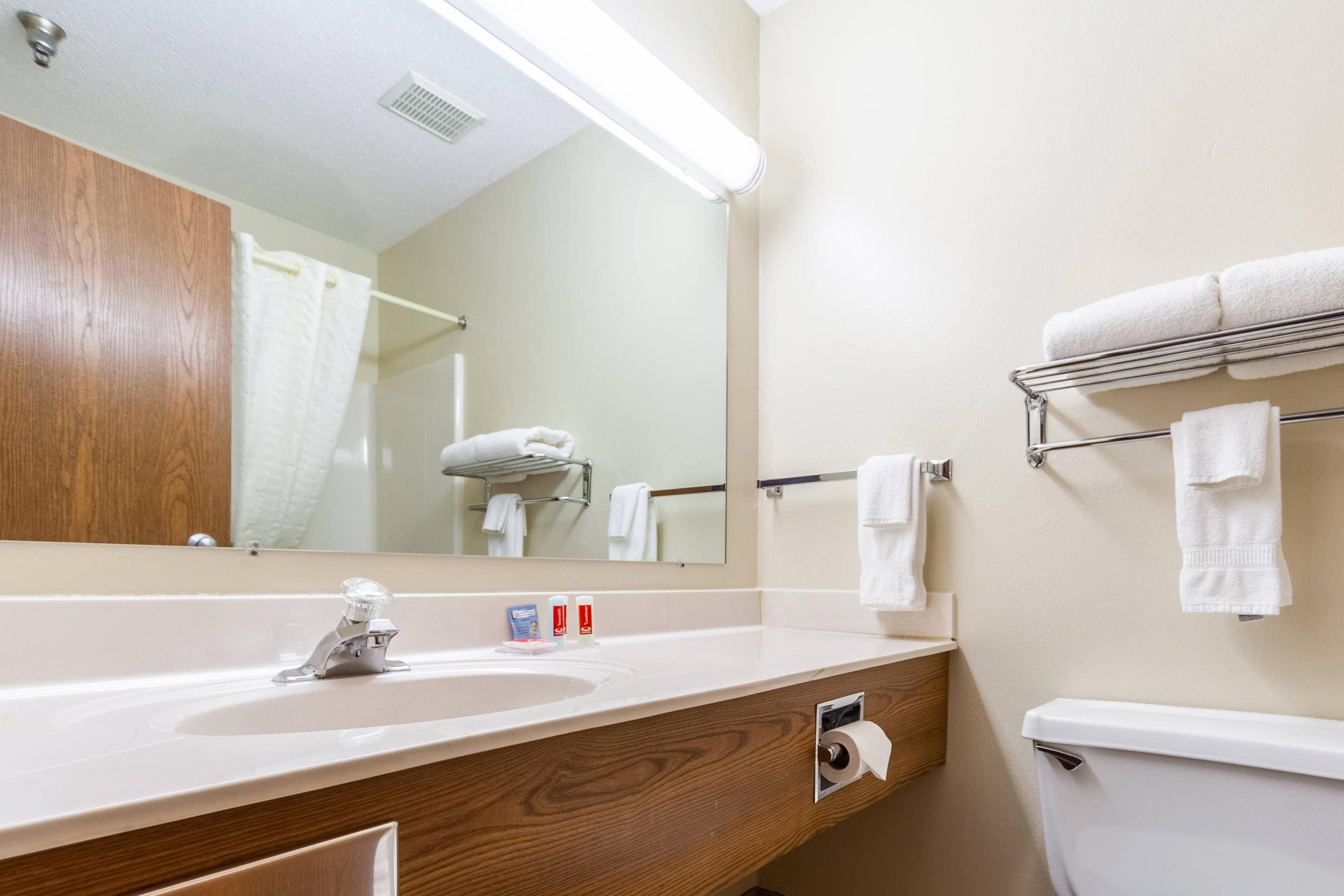 A bathroom with a wooden vanity, a sink, a mirror, a towel rack, and a toilet.