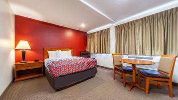 Una habitación de hotel con cama, mesita de noche, lámpara y una pequeña mesa redonda con sillas.