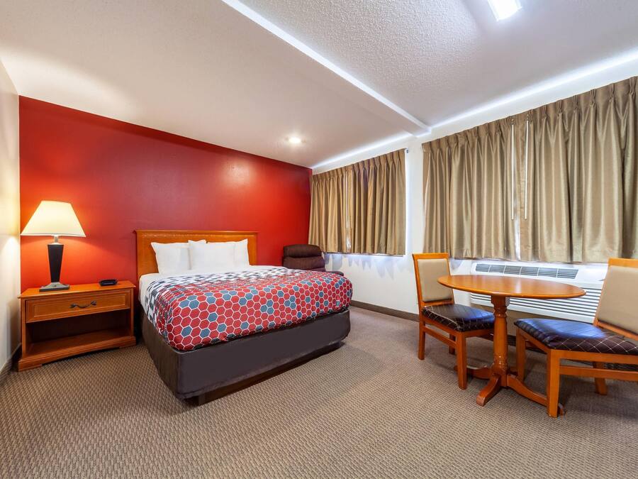 Una habitación de hotel con cama, mesita de noche, lámpara y una pequeña mesa redonda con sillas.