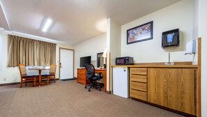 Habitación de hotel con comedor, escritorio con computadora, microondas y refrigerador pequeño.
