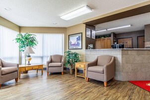 Un hall de hotel con mostrador de recepción, zona de estar y un amplio ventanal con persianas.
