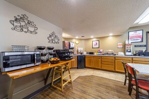 A kitchen with a microwave, coffee maker, and a coffee dispenser.