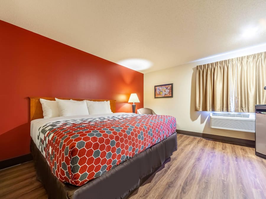 A hotel room with a bed, a desk, a lamp, a window with curtains, and a wall with a map.