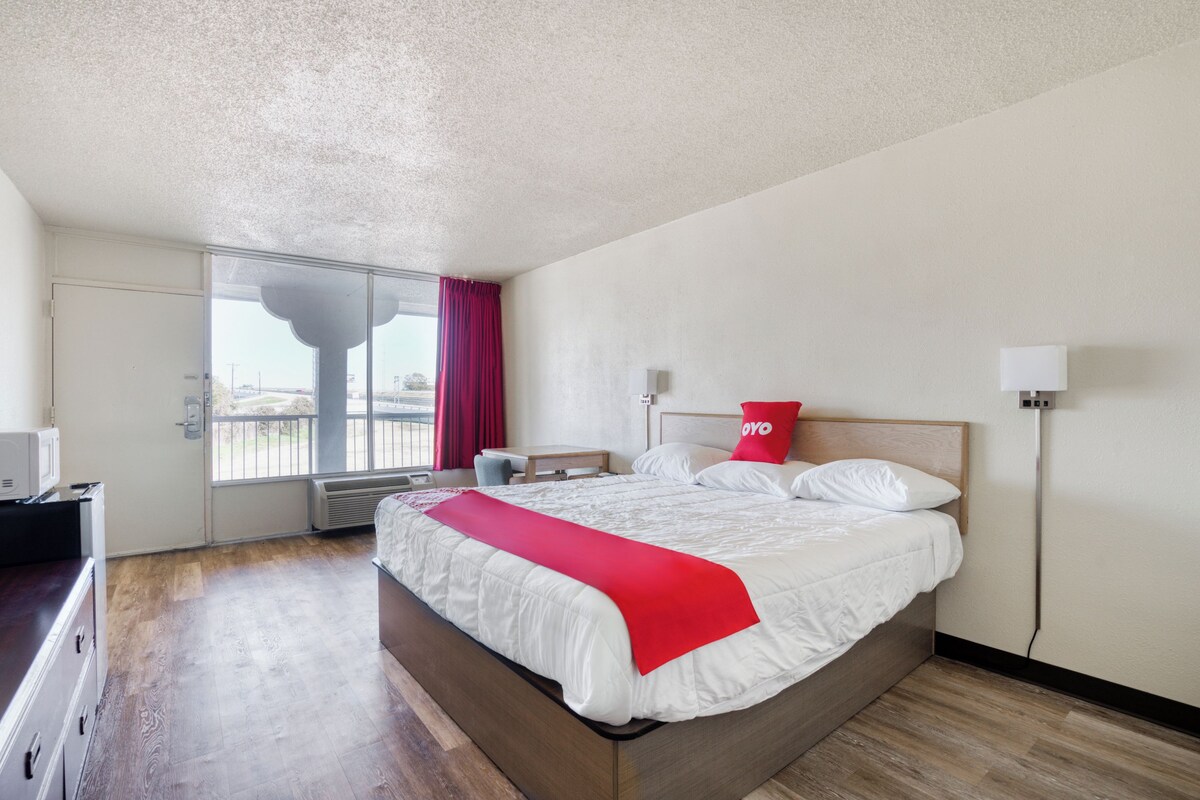 A hotel room with a bed, a desk, a chair, a window with a view, and a door.