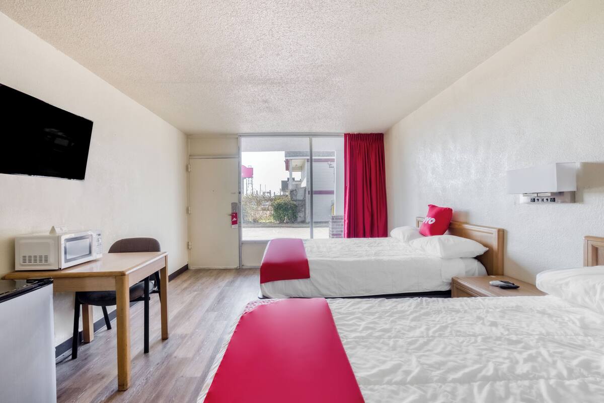 Ein Hotelzimmer mit Bett, Schreibtisch mit eingebauter Mikrowelle, Fernseher und einer Schiebetür nach draußen.