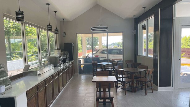 A modern kitchen with a long counter, wooden cabinets, and pendant lighting. There are multiple dining tables and chairs arranged for guests. - Wingate by Wyndham Columbia/Fort Jackson (Columbia)