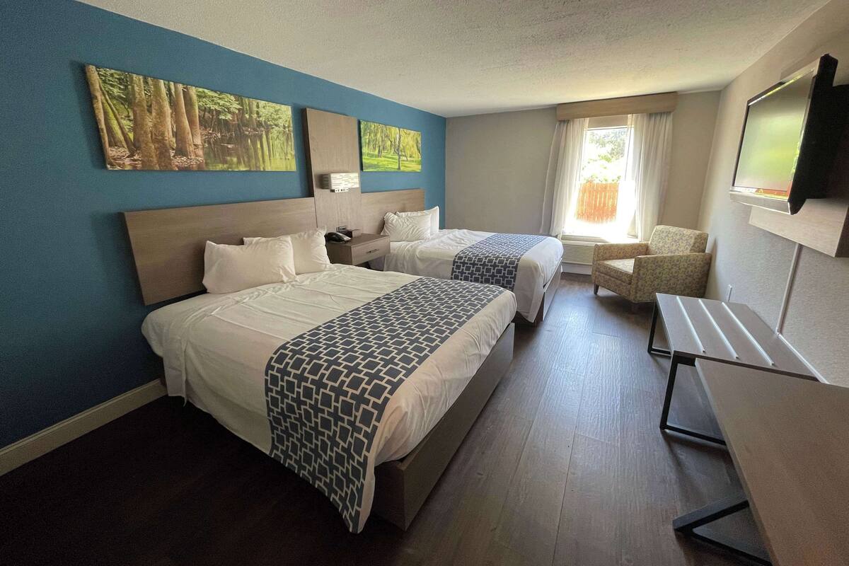 A hotel room with two beds, a desk, a chair, and a TV.