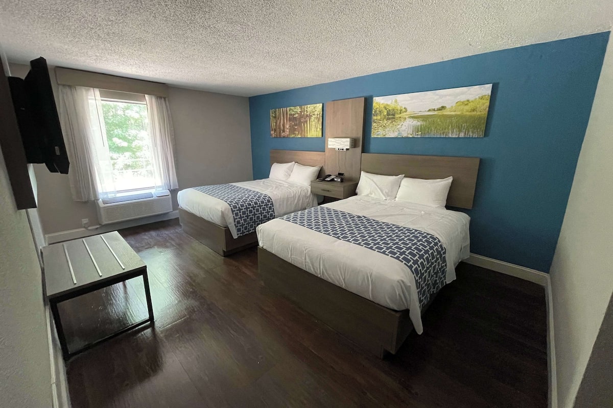 A hotel room with two beds, a small table, and a window with curtains.