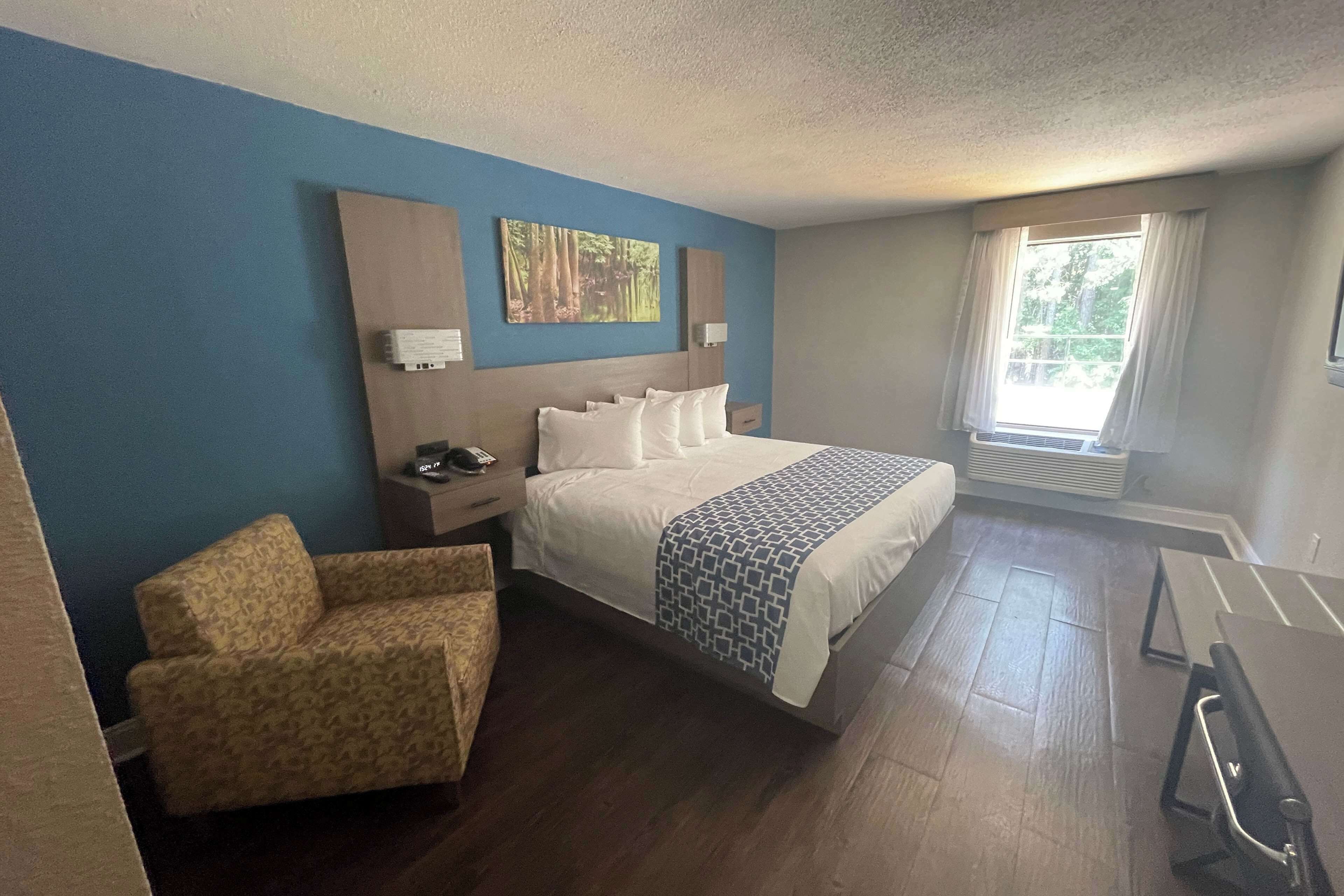 A hotel room with a bed, a chair, a desk, and a window with curtains.