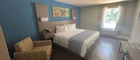 A hotel room with a bed, a chair, a desk, and a window with curtains.