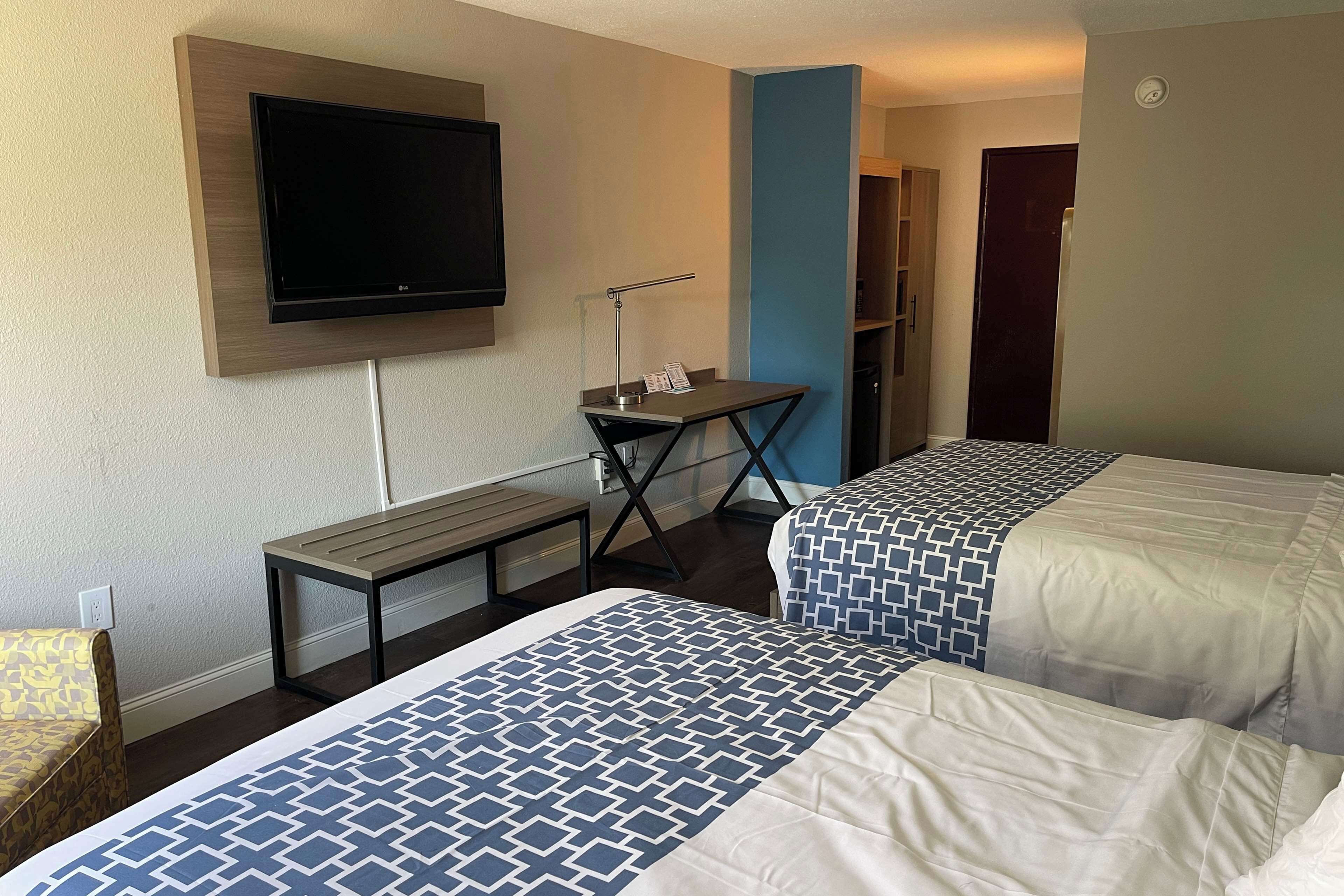 Ein Hotelzimmer mit zwei Betten, einem Schreibtisch, einem Fernseher und einem Bücherregal.