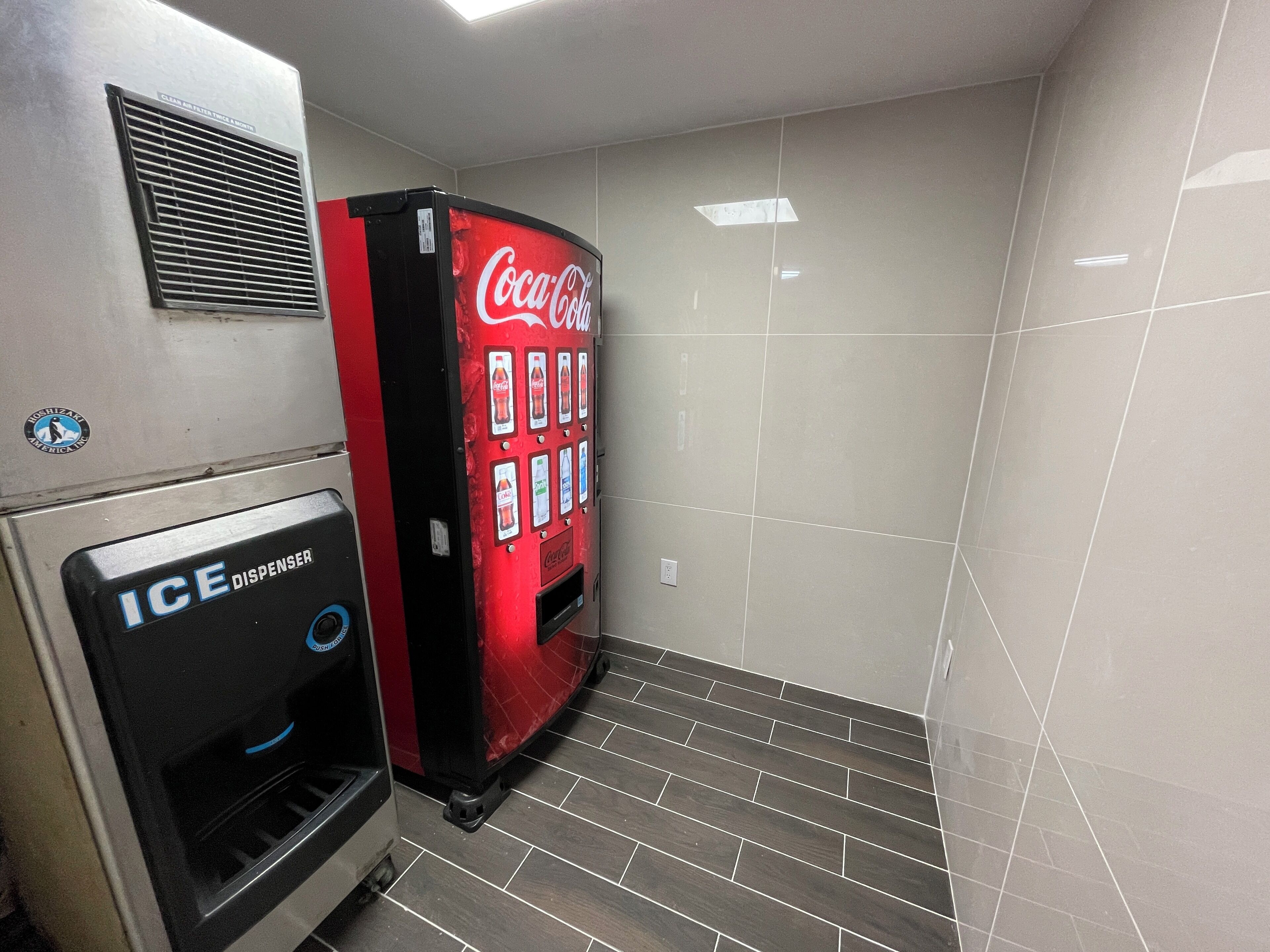 A Coca-Cola vending machine and an ICE dispenser in a restroom.