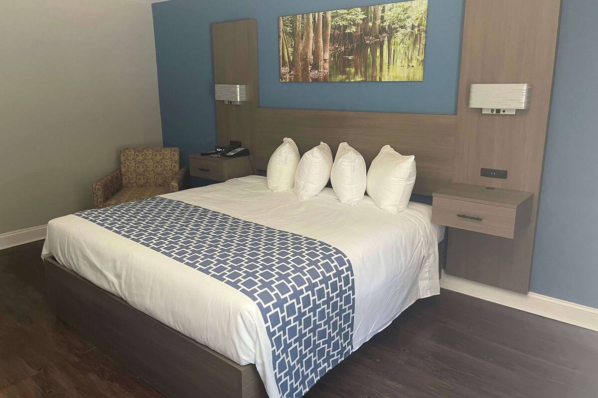 A neatly made bed with a patterned bedspread, a bedside table with a lamp, and a wall-mounted artwork.