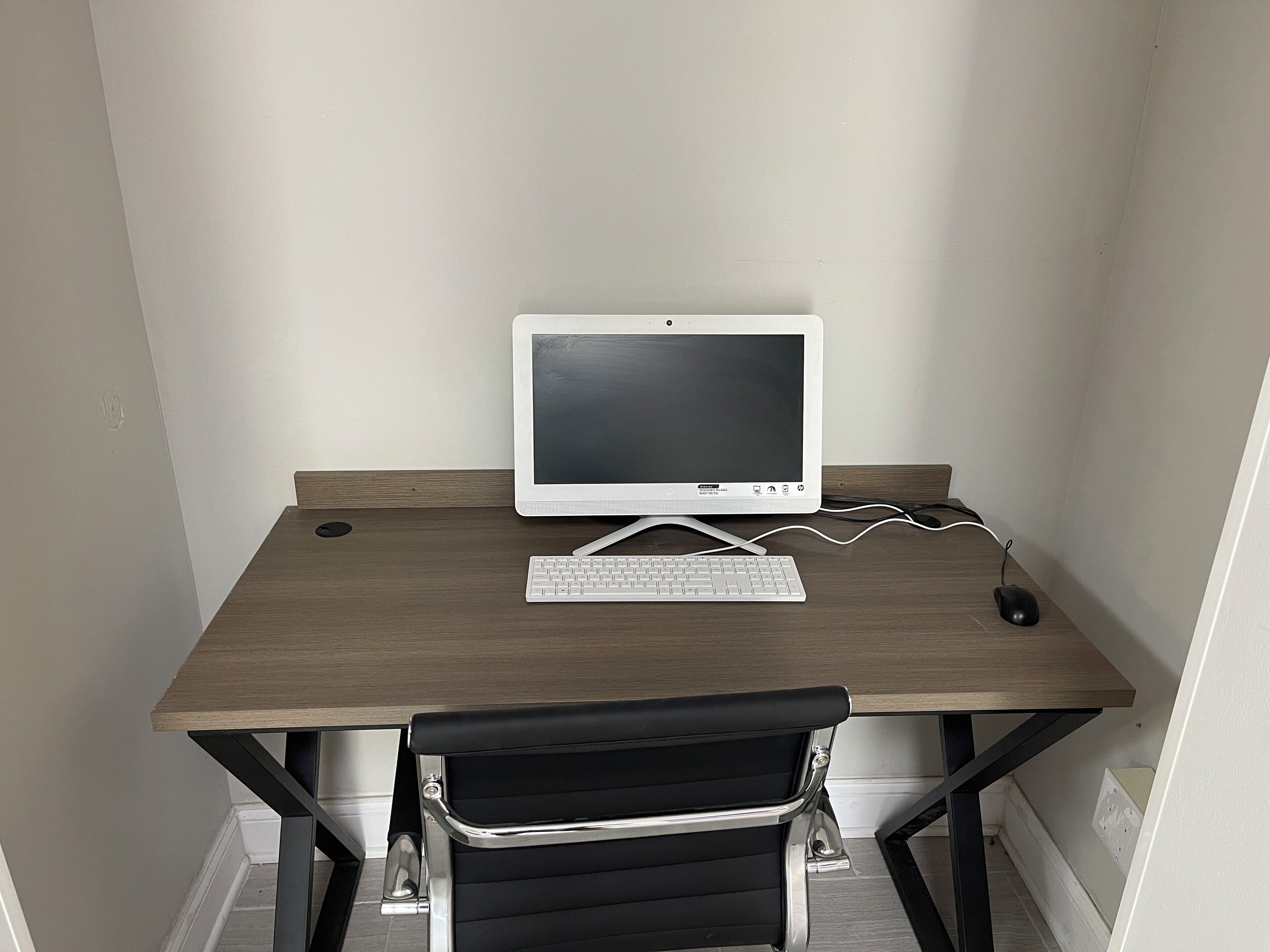 A small, square desk with a white monitor, keyboard, and mouse.