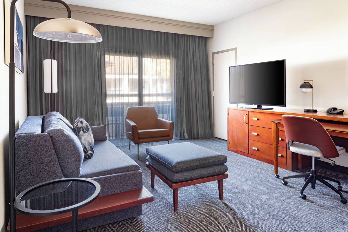 Une chambre d’hôtel équipée d’un canapé, d’un pouf, d’un bureau, d’une chaise, d’une télévision et d’une lampe.