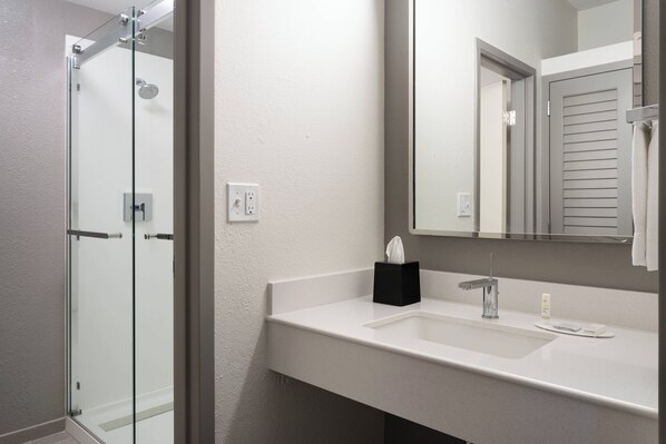 A bathroom with a glass shower enclosure, a white sink with a mirror, and a towel rack.