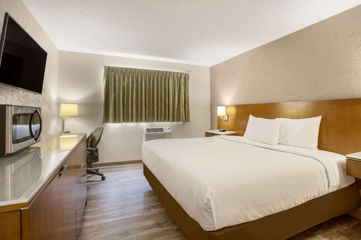 Una habitación de hotel con cama, escritorio con computadora, televisor de pantalla plana, lámpara y ventana con cortinas.