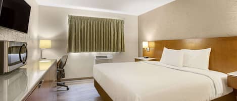 Una habitación de hotel con cama, escritorio con computadora, televisor de pantalla plana, lámpara y ventana con cortinas.