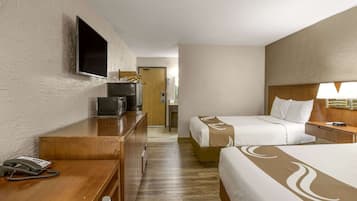 Une chambre d’hôtel avec deux lits, un bureau avec un téléphone, un téléviseur fixé au mur et une tête de lit en bois.