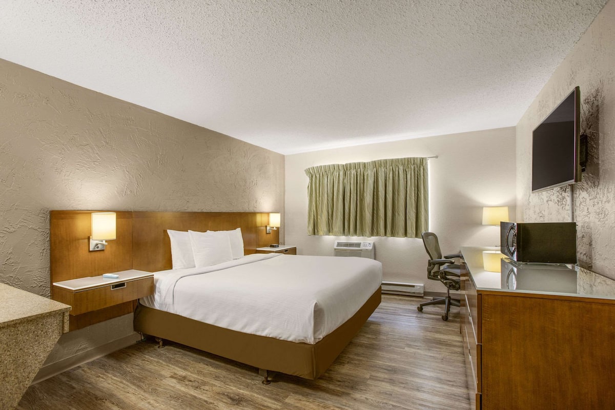 Habitación de hotel con una cama grande, un escritorio con silla, un televisor y una ventana con cortinas.