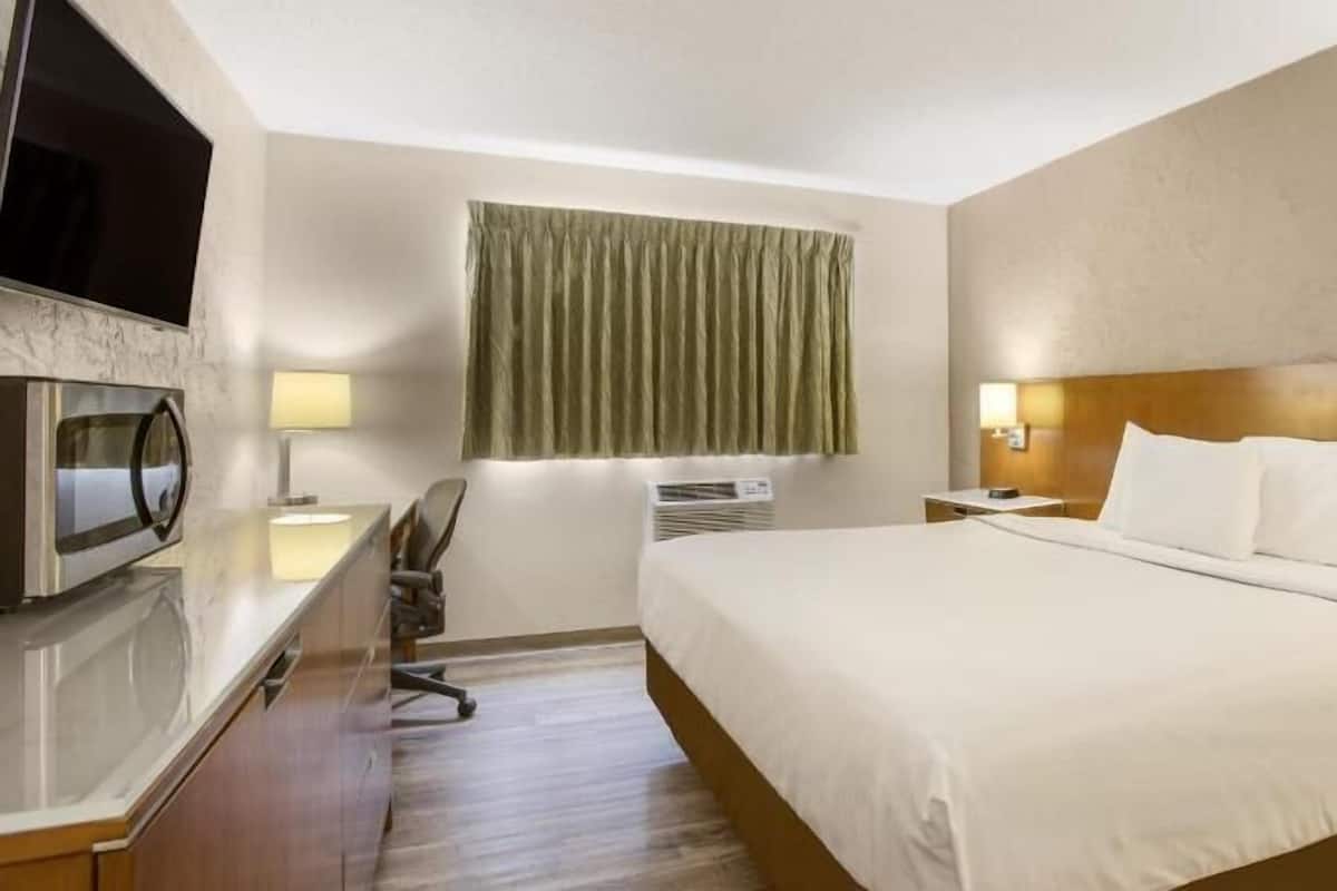 Una habitación de hotel con cama, escritorio, silla, televisor y ventana con cortinas.