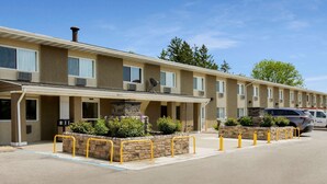 A motel with a row of rooms, a covered parking area, and a stone planter with plants.