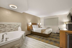 Habitación de hotel con una bañera grande, una cama con cabecera, lámparas de noche, un televisor y un microondas.