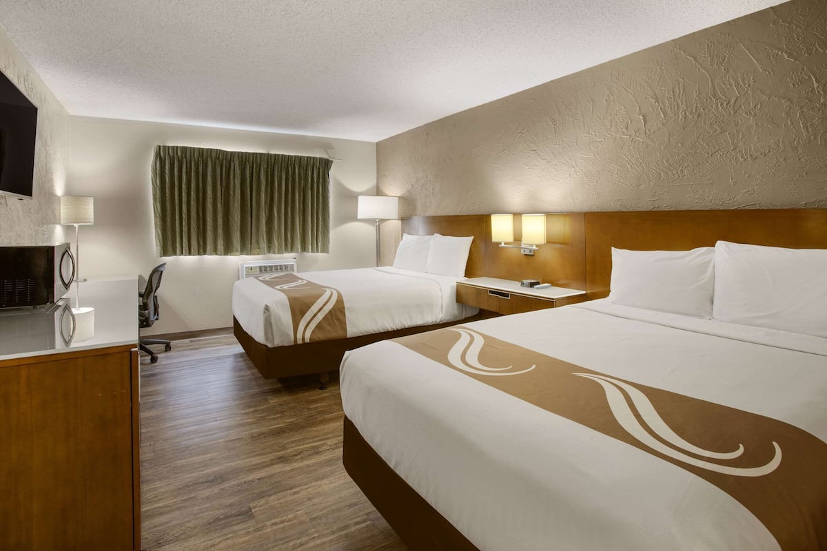 Habitación de hotel con dos camas, un escritorio, una silla, un televisor y una ventana con cortinas.