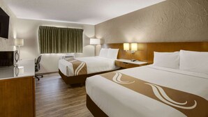 A hotel room with two beds, a desk, a chair, a TV, and a window with curtains.