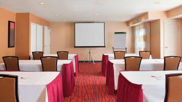 A conference room with tables, chairs, a projector screen, and a carpeted floor.