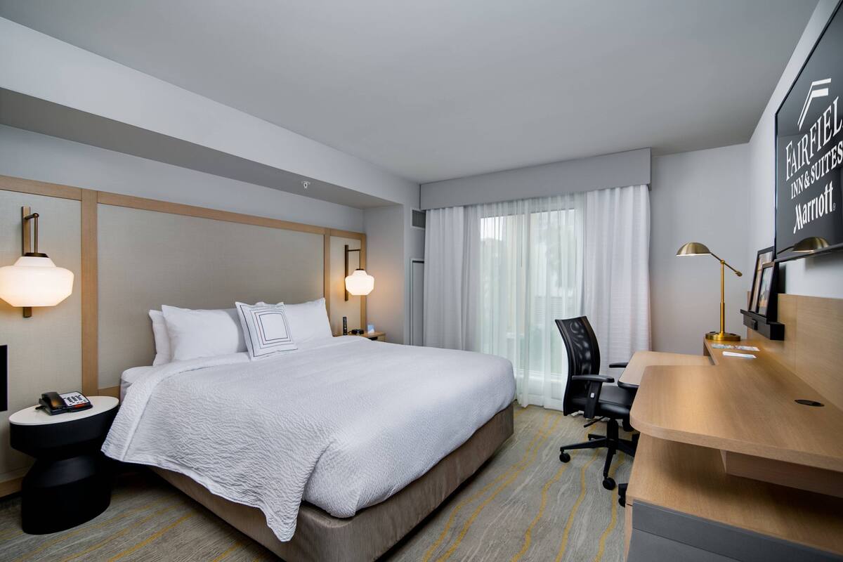Habitación de hotel con una cama grande, un escritorio y una silla. Hay un teléfono en la mesita de noche y una lámpara en el escritorio.