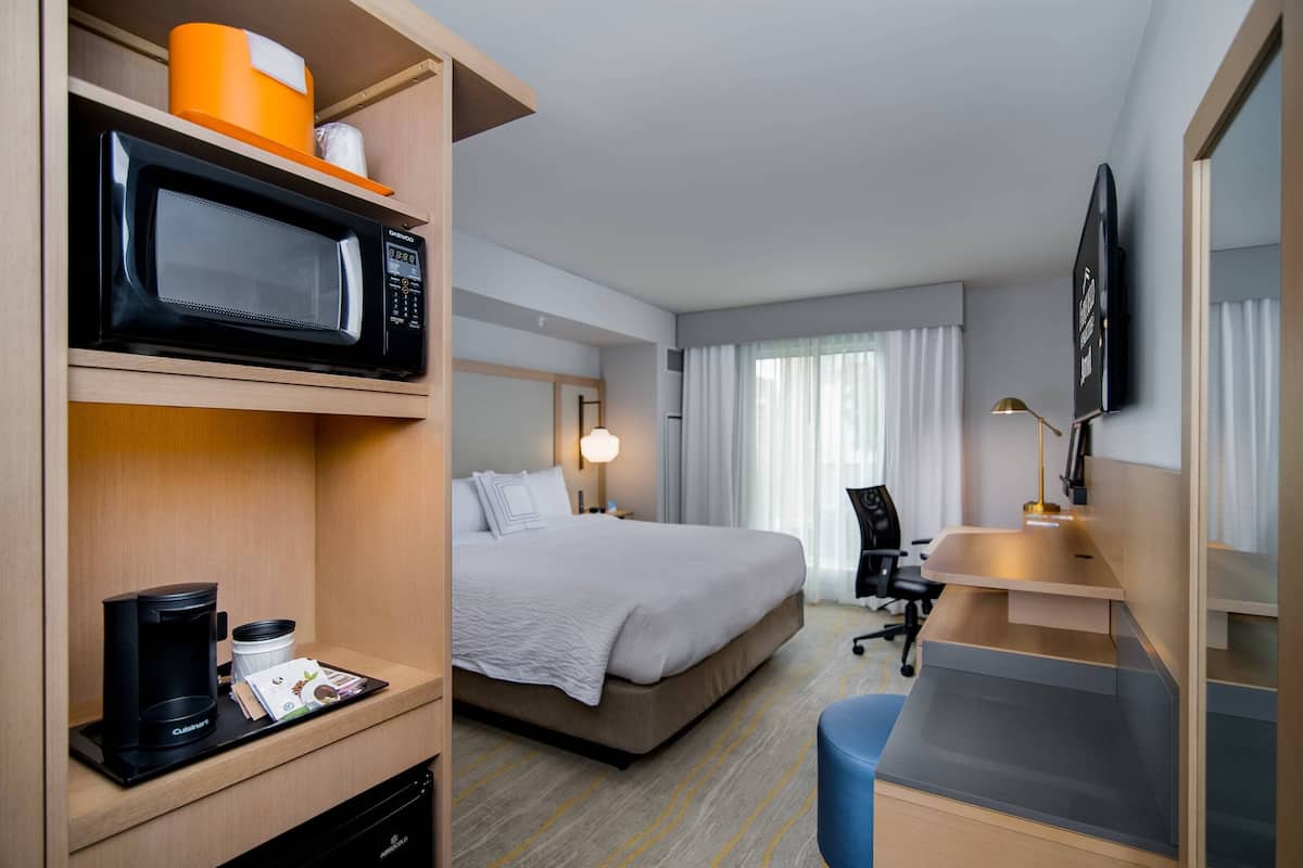 Una habitación de hotel con cama, escritorio, microondas, cafetera y televisión.
