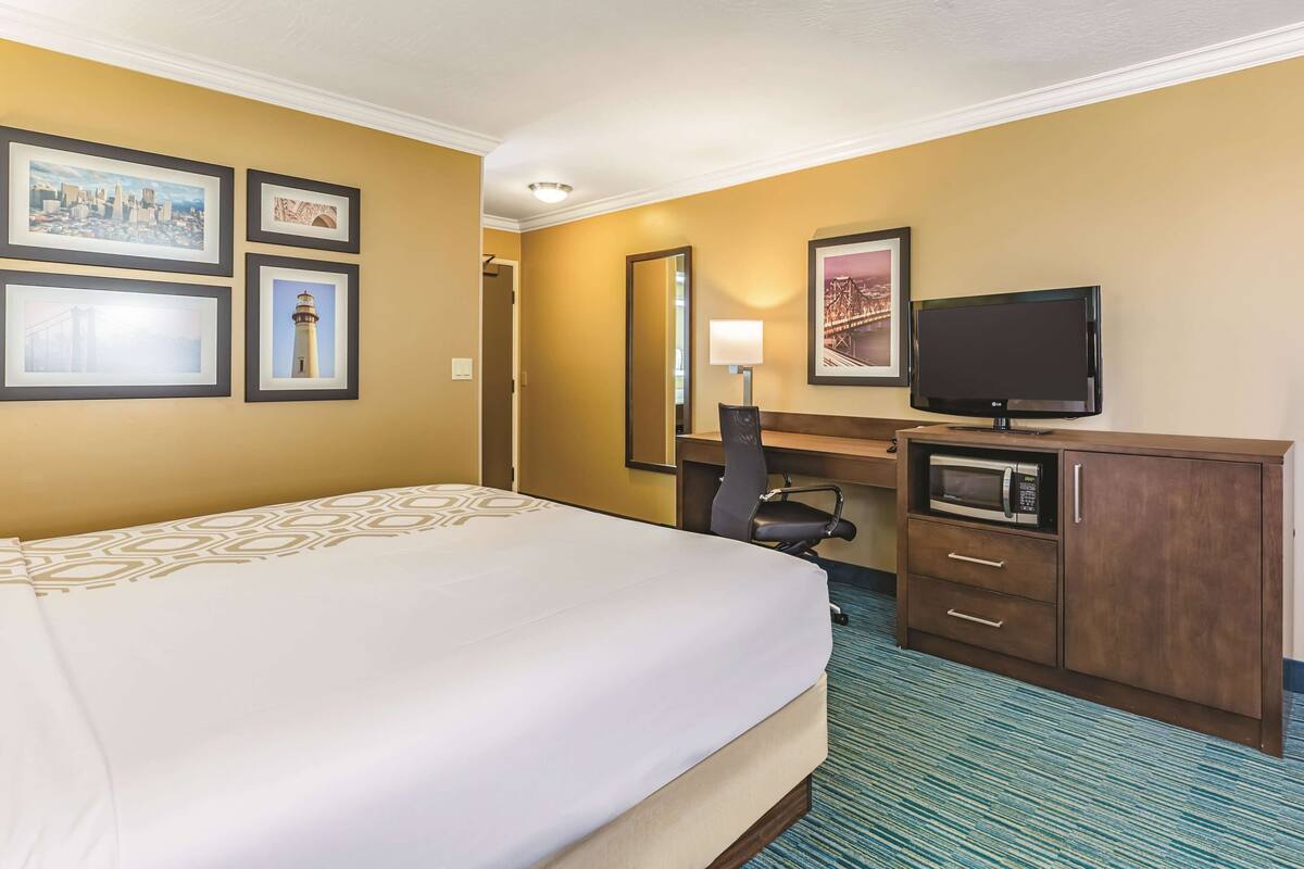 Una habitación de hotel con cama, escritorio, computadora, televisor y microondas.