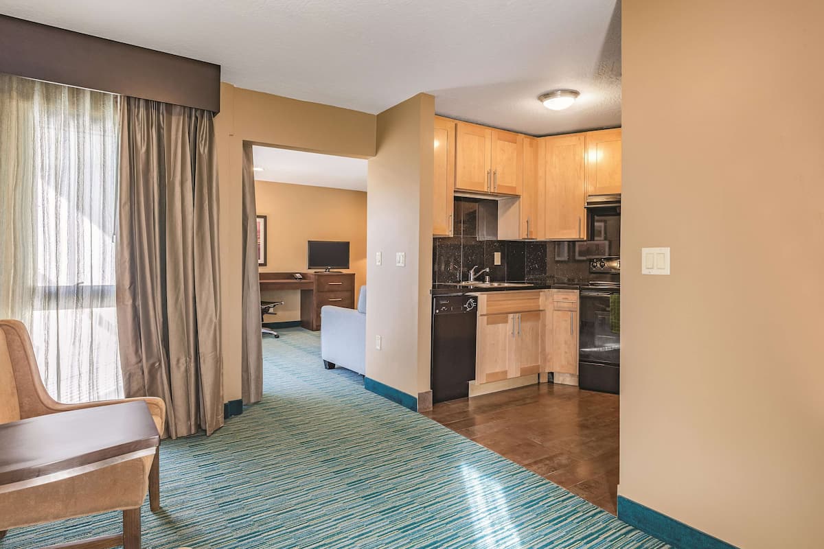 Habitación de hotel con escritorio, silla y vista al pasillo que lleva a la cocina.