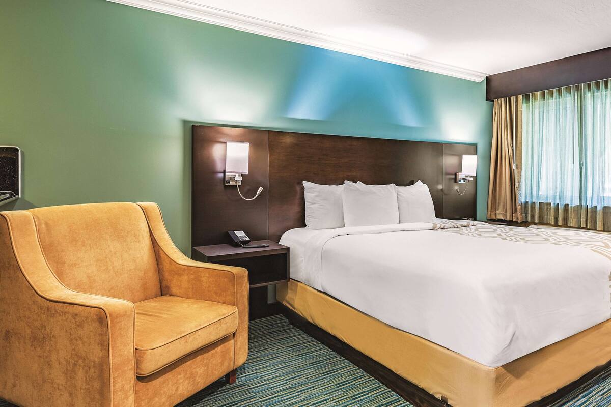 A hotel room with a large bed, a nightstand with a phone, a chair, and a wall-mounted light.