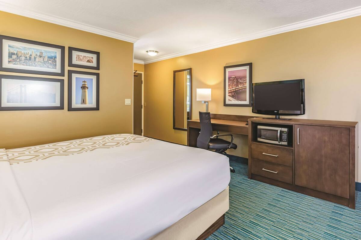 A hotel room with a bed, a desk with a TV, a microwave, and framed pictures on the wall.