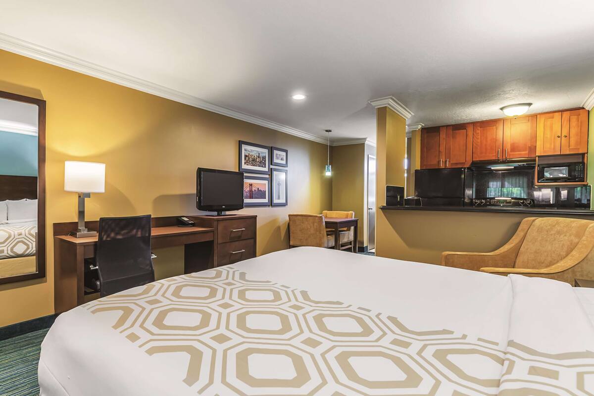 Habitación de hotel con cama, escritorio, silla, televisor y kitchenette.