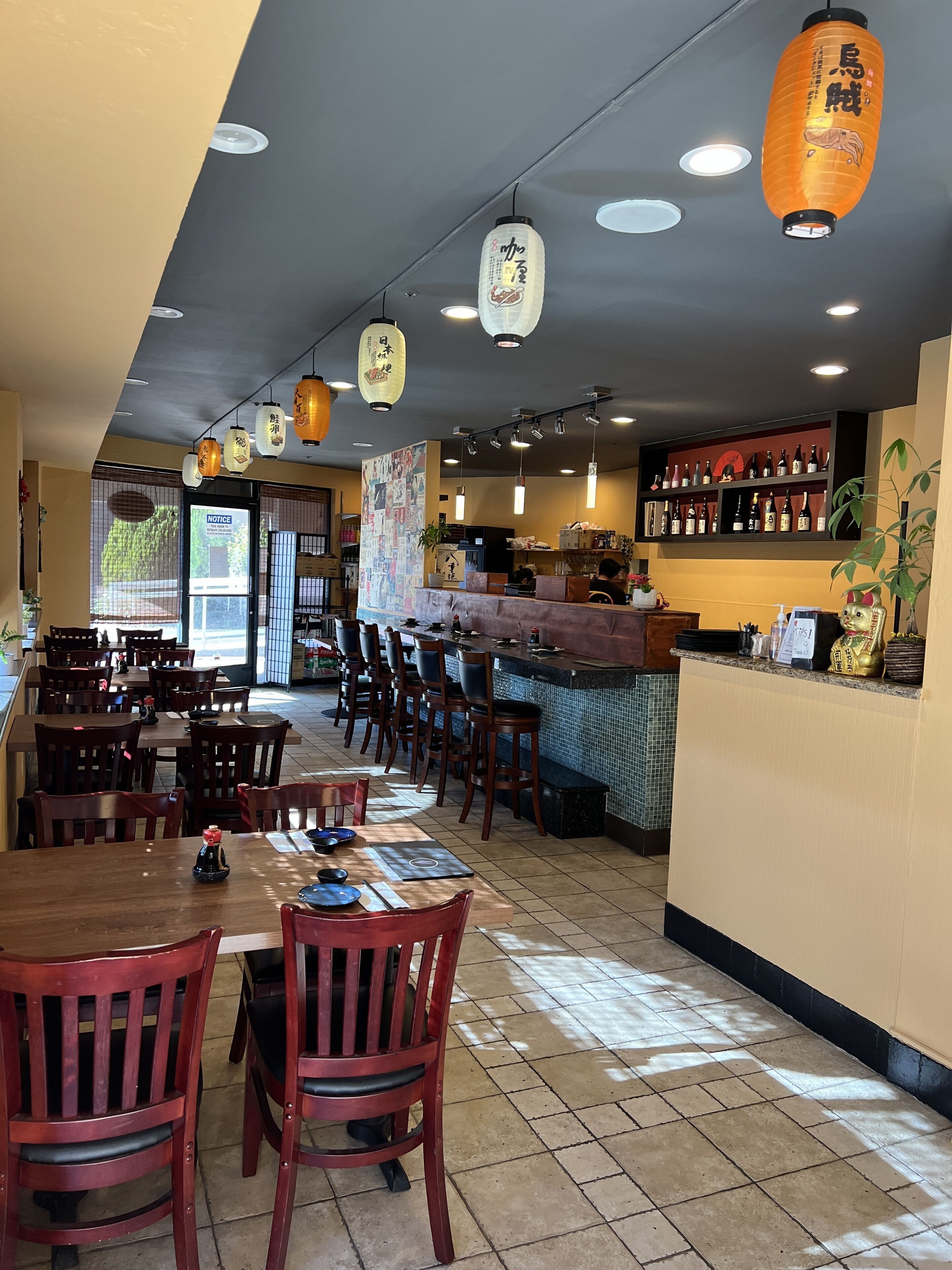 Interno di un ristorante con tavoli e sedie in legno, un bancone con il menu e lanterne appese.